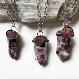 May include: Three silver chain necklaces with red and white crystal pendants. Each pendant is a pointed crystal with a silver bezel setting around a red gemstone.