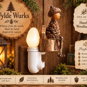 May include: A wall plug-in night light featuring a white plastic base with a glowing bulb and a decorative figure made of a pinecone and acorn sitting on a small wooden log. The text Wylde Wurks, One of a Kind Handmade Woodland Hook, and other labels appear.