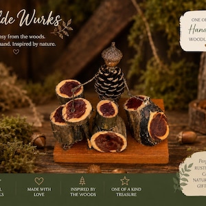 May include: A figurine crafted from natural materials, featuring a pinecone body and acorn cap head, positioned behind a miniature drum set made of small wood slices with dark red centers, all mounted on a rectangular wooden base.