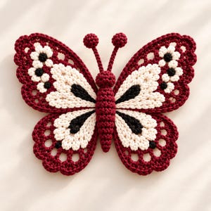 May include: A crocheted butterfly wall hanging featuring a central body and two antennae in deep burgundy. The wings are patterned with cream-colored sections, black accents, and a scalloped burgundy border with openwork detailing.