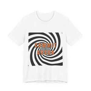 May include: A white short-sleeved t-shirt featuring a square graphic on the chest. The graphic displays a black and white spiral pattern with the orange text COMMIT ARSON centred over the design in a bold, sans-serif capital letter font.