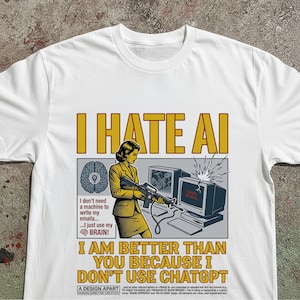Pode incluir: Uma t-shirt branca com uma impressão gráfica com o texto I HATE AI no topo e I AM BETTER THAN YOU BECAUSE I DON'T USE CHATGPT na parte inferior. A ilustração mostra uma pessoa a apontar uma espingarda a um monitor com um ícone de cérebro.