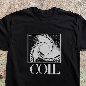 Puede incluir: Una camiseta negra de manga corta con un gráfico cuadrado en el pecho. El gráfico muestra un diseño de escalera de caracol en blanco y negro de alto contraste. Debajo del gráfico, la palabra COIL está impresa en letras mayúsculas blancas.