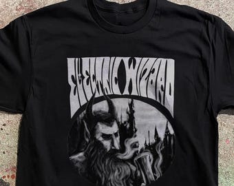May include: A black short-sleeve t-shirt featuring a graphic print in shades of gray. The design includes the text "ELECTRIC WIZARD" in a stylized font above a circular illustration of a bearded, horned figure holding a smoking chalice.
