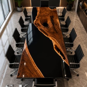 Könnte beinhalten: Ein großer rechteckiger Konferenztisch mit einer Baumkanten-Holzplatte mit ausgeprägter Maserung und einem dunklen Astloch, kombiniert mit einem glänzenden schwarzen Epoxidharz-Fluss. Der Tisch ist von zwölf schwarzen Bürostühlen aus Leder umgeben.