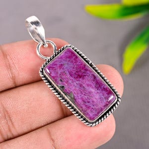 Peut inclure: Un pendentif rectangulaire orné d'une pierre précieuse magenta vif avec des inclusions naturelles. La pierre est sertie dans un cadre en argent poli avec une bordure torsadée et comprend une bélière en argent sur le dessus pour la chaîne.