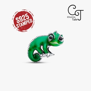 May include: A silver charm shaped like a chameleon with vibrant green enamel detailing, black eyes, and a textured spine. The charm features a red circular stamp reading S925 STAMPED and a logo for Charms Tale in the upper right corner.
