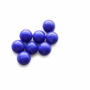 May include: A collection of eight small, round, smooth, and opaque cobalt blue cabochons. Each piece features a polished, domed surface with a consistent circular shape and a vibrant, solid blue color, arranged in a loose cluster on a white surface.