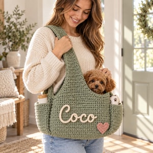May include: A sage green crocheted pet carrier bag featuring a wide shoulder strap and two side pockets. The front is decorated with the white cursive name Coco and a small pink crocheted heart. A small brown puppy is sitting inside the bag.
