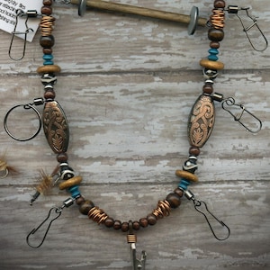 May include: A handcrafted fishing lanyard with a black neckband, wooden beads, and copper accents. Features a cork, swivel snaps, and a tag that reads "Echo Canyon Lanyards". The lanyard is designed to hold fishing accessories.