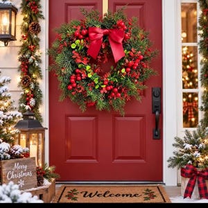 Op de afbeelding: Een ronde kerstkrans met groene dennennaalden, felrode bessen en een grote rode satijnen strik, bevestigd aan een rode voordeur. Voor de deur ligt een rechthoekige bruine deurmat met het woord Welcome in zwarte letters op de mat gedrukt.