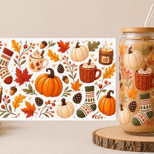 Peut inclure: Un verre transparent avec un couvercle en bambou et une paille en verre, contenant une boisson beige. Le verre présente un motif imprimé coloré de citrouilles orange et blanches, de feuilles d'automne, de pommes de pin, de glands et de tasses.