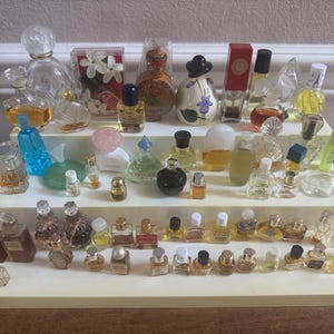 May include: A display of miniature perfume bottles in diverse shapes and sizes, arranged on a tiered stand. The bottles are clear, coloured, and opaque, with various caps and designs. Some bottles contain visible liquid, creating a vintage aesthetic.