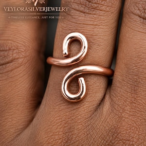 Peut inclure: Une bague bypass couleur or rose avec une finition lisse et polie. Le design se compose d'un fil métallique continu qui se courbe en deux extrémités ouvertes et arrondies se chevauchant légèrement au centre, créant un effet de spirale.