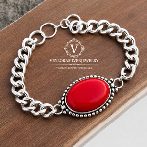 Pode incluir: Uma pulseira de elos de prata com uma grande pedra vermelha lisa de formato oval, engastada numa moldura de prata com contas. A pulseira inclui um fecho circular e apresenta o texto VEYLORASILVERJEWELRY TIMELESS BEAUTY, PURE SILVER.