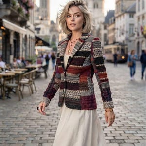 Puede incluir: Una chaqueta de manga larga con un patrón de punto multicolor en tonos burdeos, negro, gris y crema, sobre un vestido liso de color crema. La chaqueta presenta solapas de muesca, cierre frontal de botones y puños texturizados en las mangas.
