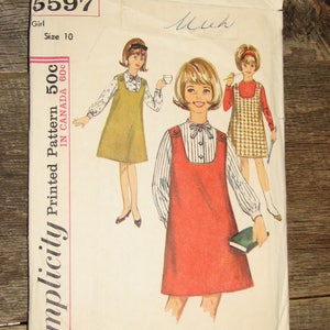May include: A vintage Simplicity pattern envelope with illustrations of girls' dresses. The envelope is off-white and displays the text "5597 Girl Size 10" and "Simplicity Printed Pattern". The illustrations show girls in different dresses.