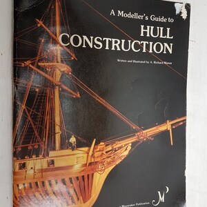 May include: A book titled "A Modeller's Guide to Hull Construction" with a black cover. The cover features a detailed illustration of a wooden ship model. The author's name is A. Richard Mansir.