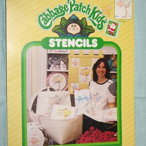 Peut inclure: Un ensemble de pochoirs Cabbage Patch Kids vintage. L'emballage est jaune avec une bordure verte et présente le logo Cabbage Patch Kids et le mot "STENCILS". L'ensemble comprend des feuilles de pochoirs prédécoupées de 21,6 cm x 28 cm. L'image montre des motifs pochoirs sur divers articles.