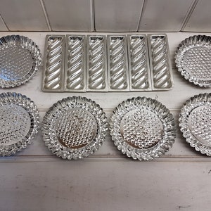 May include: A selection of vintage silver baking moulds. The collection includes round tart tins with fluted edges and textured centres, alongside rectangular loaf tins with a twisted design. These moulds are ideal for baking.