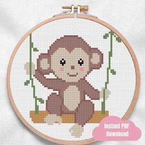 Könnte beinhalten: Ein Kreuzstichmuster in einem hölzernen Stickrahmen mit einem braunen Affen mit hellbeigem Gesicht und Bauch, rosa Wangen und schwarzen Augen, der auf einem braunen Ast zwischen zwei grünen Ranken auf weißem Gitterstoff sitzt.
