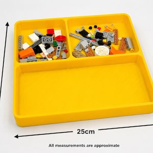 May include: A bright yellow plastic sorting tray with three compartments. Two smaller top sections contain various colorful plastic building bricks, while the bottom section is empty. The tray measures 25cm by 25cm as indicated by arrows.