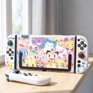 Könnte beinhalten: Eine weiße tragbare Spielkonsole und ein abnehmbarer Controller mit einer farbenfrohen Collage verschiedener Zeichentrickfiguren. Der Bildschirmbereich der Konsole zeigt ein lebhaftes Muster aus Kreaturen, während die weißen Controller Tasten, Joysticks und kleine Grafiken zum Thema Pokémon enthalten.