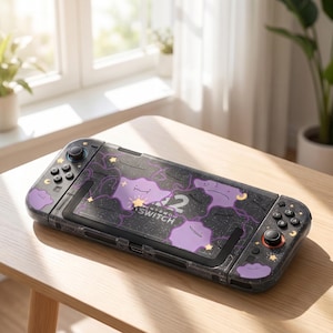 Könnte beinhalten: Eine schwarze Nintendo Switch Konsole mit einer Schutzhülle, die ein violettes Charakter-Muster, kleine gelbe Sterne und Mondsicheln aufweist. Die Konsole hat schwarze Tasten, einen schwarzen Joystick und einen rot akzentuierten Joystick.