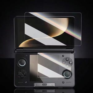 Könnte beinhalten: Eine schwarze tragbare Spielkonsole mit zwei Bildschirmen und zwei transparenten Displayschutzfolien, die vor dem oberen und unteren Bildschirm positioniert sind. Das Gerät verfügt über ein Steuerkreuz, zwei Analogsticks und vier Aktionstasten X, Y, A, B.