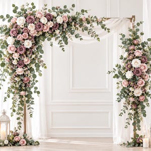May include: A wedding arch decorated with artificial flowers in shades of dusty rose, mauve, and cream, accented with green eucalyptus leaves and white sheer fabric. Two white metal lanterns with lit candles sit at the base of the arch structure.