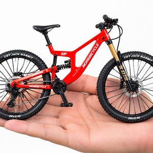 May include: A miniature red mountain bike model featuring black tyres with CST Jack Rabbit branding, a rear suspension coil, and the text Morebicycle printed on the frame. The bicycle has black handlebars, a black seat, and disc brakes.