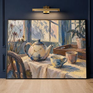 Puede incluir: Un óleo enmarcado que muestra una tetera blanca con líneas de reparación kintsugi doradas, una taza de té estampada y una taza lisa sobre un mantel blanco. La escena se sitúa junto a una ventana con marcos azules y luz suave.