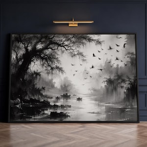 May include: A black and white landscape painting in a thin black frame depicting a misty river scene with silhouetted trees, small boats on the water, and a flock of birds flying across the sky, mounted on a dark blue panelled wall.