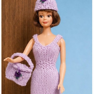 Peut inclure: Une poupée portant une robe tricotée à la main de couleur lavande avec un chapeau assorti et un petit sac à main. Le chapeau et le sac à main sont tous deux ornés d'une fleur violette foncée. La poupée a les cheveux bruns et porte des chaussures claires.
