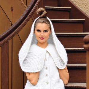 May include: A white knitted sleeveless cardigan featuring a large hood and a front button closure with four circular buttons. The garment is crafted from a soft, fuzzy yarn with a ribbed texture, providing a structured yet comfortable fit.