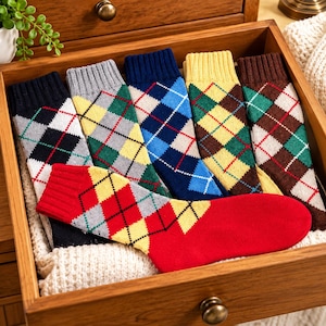 Op de afbeelding: Een collectie van zes paar sokken met een klassiek argyle-ruitpatroon in diverse kleurcombinaties waaronder rood, geel, blauw, groen, grijs, zwart en bruin, netjes gerangschikt in een houten lade met een geribbelde boord.