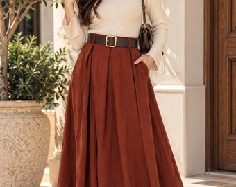 Peut inclure: Une longue jupe plissée couleur rouille avec une ceinture marron foncé dotée d'une boucle dorée, associée à un haut beige à manches longues et col montant côtelé, des bottines marron foncé et un sac à bandoulière marron.