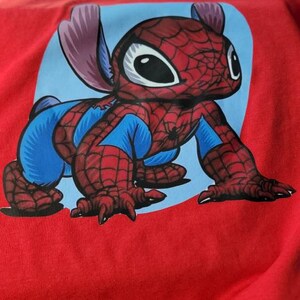Puede incluir: Camiseta roja con un personaje de dibujos animados azul y rojo vestido de Spiderman. El personaje tiene ojos grandes y una expresi&oacute;n amigable.