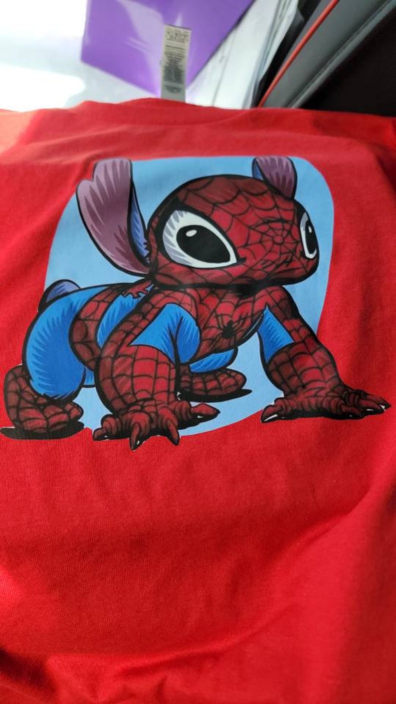 Puede incluir: Camiseta roja con un personaje de dibujos animados azul y rojo vestido de Spiderman. El personaje tiene ojos grandes y una expresi&oacute;n amigable.