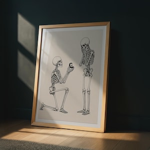 May include: A framed wall art print featuring a black line drawing on a beige background. The illustration depicts two human skeletons, one kneeling and holding an open ring box toward the other, who stands with hands clasped near the face.