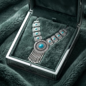 May include: A silver-toned necklace featuring a large circular pendant with a central turquoise stone, surrounded by intricate radial metalwork and a fringe of small silver dangles. The chain consists of repeating circular links with turquoise accents.