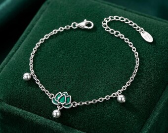 May include: A silver chain bracelet featuring a central lotus flower charm with green enamel detailing. The bracelet includes three small silver spherical beads spaced along the chain and a lobster claw clasp with an oval tag at the end of the extender.