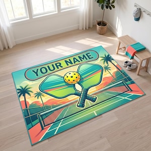 Può includere: Un tappeto rettangolare che raffigura un vivace campo da pickleball al tramonto con palme, una rete, due racchette incrociate e una pallina gialla. Il testo "YOUR NAME" è stampato in un carattere grande e in grassetto nella parte superiore.