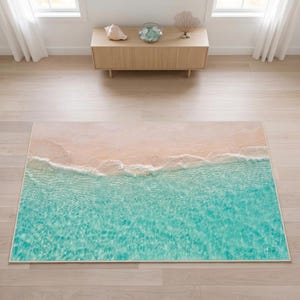 Könnte beinhalten: Ein rechteckiger Teppich mit einem hochauflösenden Fotodruck eines tropischen Strandabschnitts. Das Design zeigt hellbeigen Sand, der auf klares türkisfarbenes Meerwasser trifft, mit weißen Schaumkronen an der Küstenlinie.