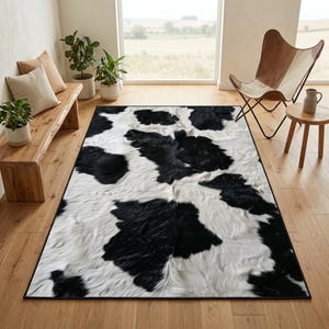 May include: A rectangular area rug featuring a black and white cowhide pattern with a textured, fur-like appearance. The rug has a distinct dark border and is laid flat on a light-colored wooden floor, showcasing irregular patches of black and white.
