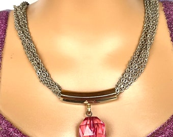May include: A gold chain necklace with multiple strands and a pendant featuring a large, faceted, pink crystal and a smaller, green crystal.