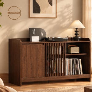 May include: A dark brown wooden media console featuring a solid cabinet door on the left and a slatted sliding door on the right. The unit includes open shelving filled with vinyl records, a turntable on top, and a small radio on the shelf.