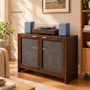 May include: A dark brown wooden media console with two doors featuring dark mesh panels and gold handles. A record player with a clear dust cover sits on top, flanked by two light blue speakers. The text BloomShopUS is visible.