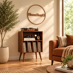 May include: A brown wooden record player stand with four tapered legs, featuring an open top shelf holding a turntable, headphones, and books, and a lower section with four vertical dividers for vinyl records, topped by a circular wall sign.