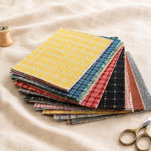 May include: A stack of rectangular fabric swatches featuring various plaid and checkered patterns in yellow, blue, red, black, orange, and gray. The fabric pieces are layered on top of each other, displaying a variety of woven textures and colors.